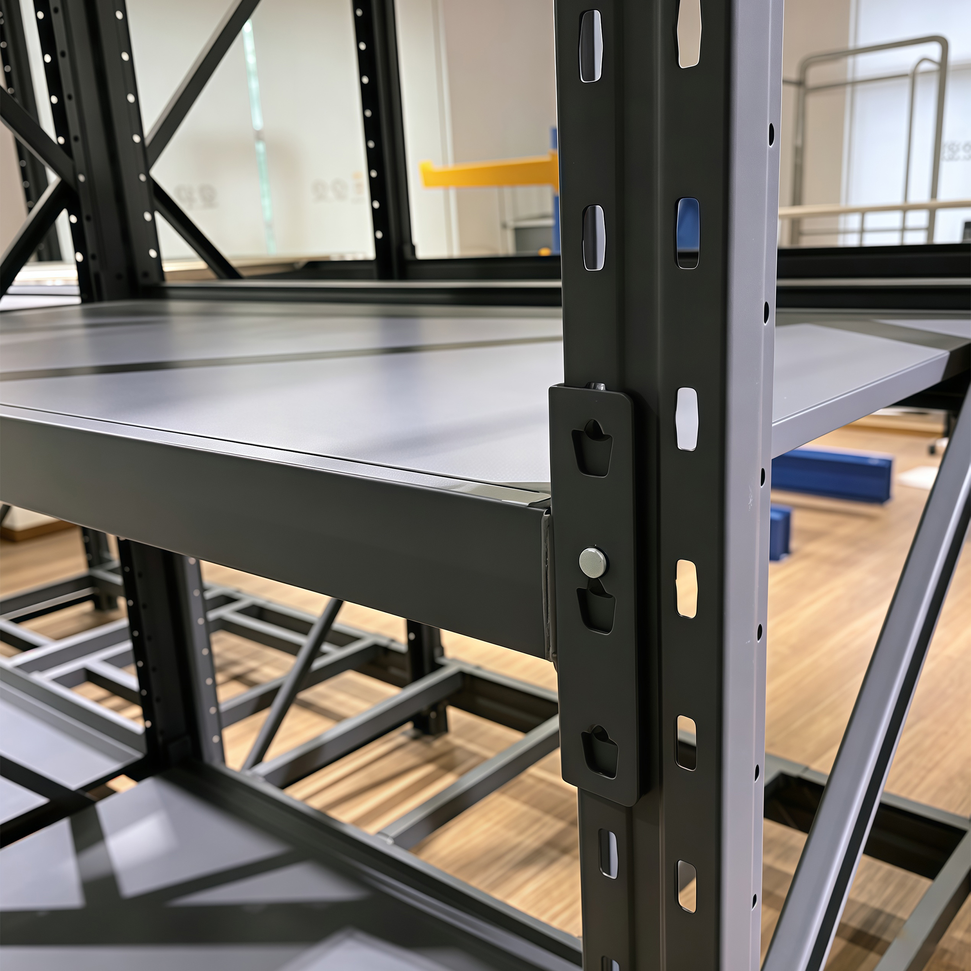 Close-up of a dark steel storage rack showing a slotted upright, a shelf panel and a bracketed beam connection